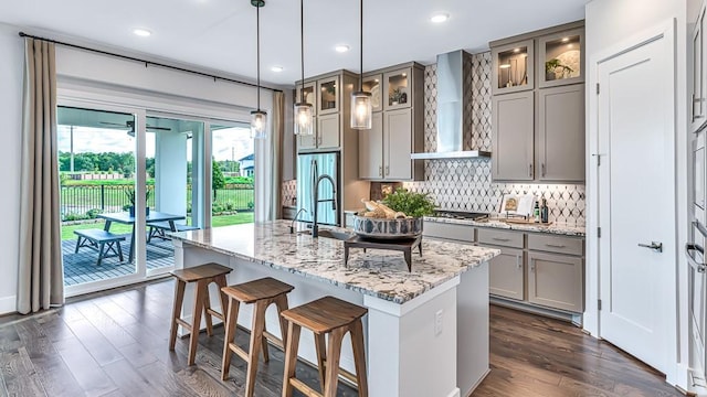 kitchen with decorative backsplash, stainless steel gas cooktop, a center island with sink, gray cabinetry, and wall chimney exhaust hood