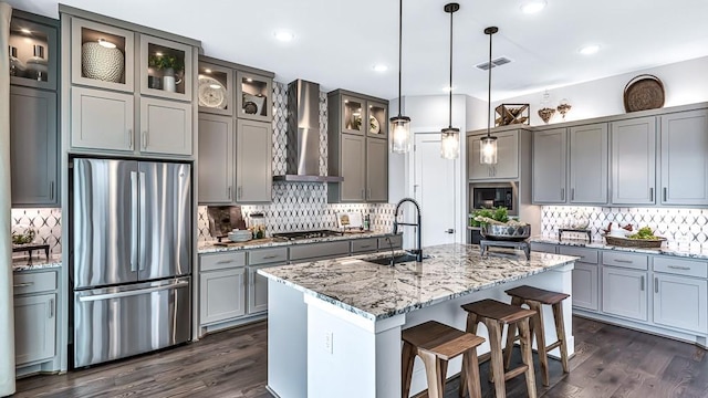 kitchen featuring appliances with stainless steel finishes, a sink, wall chimney exhaust hood, decorative backsplash, and gray cabinetry