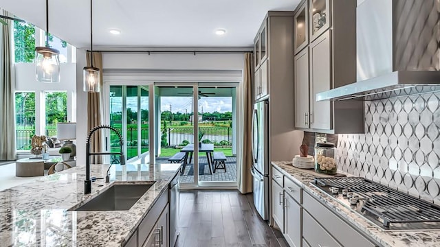 kitchen featuring wall chimney range hood, decorative backsplash, a sink, light stone counters, and stainless steel appliances