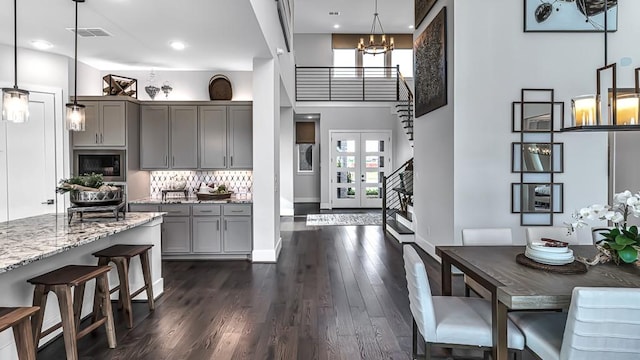 kitchen featuring visible vents, a high ceiling, gray cabinets, light stone counters, and dark wood finished floors