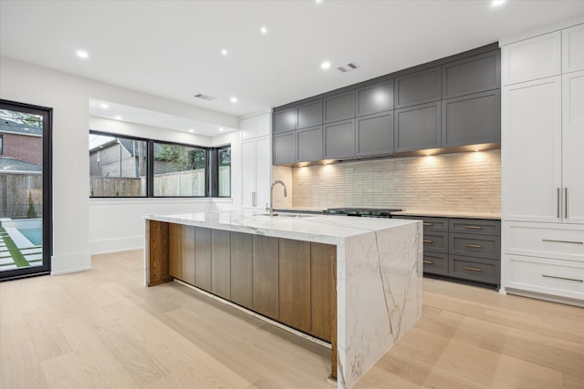 1550 Gardenia Dr, Houston, TX 77018 - kitchen with a sink, light wood-style floors, light stone counters, tasteful backsplash, and a center island with sink
