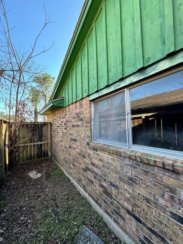 view of side of home with brick siding, board and batten siding, and fence