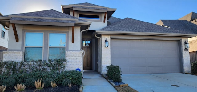 prairie-style house with brick siding, a garage, a shingled roof, and concrete driveway