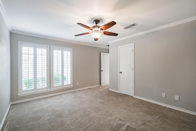 spare room featuring visible vents, ornamental molding, carpet floors, baseboards, and a ceiling fan