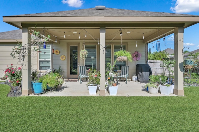 rear view of house featuring a yard, a patio, and a shingled roof