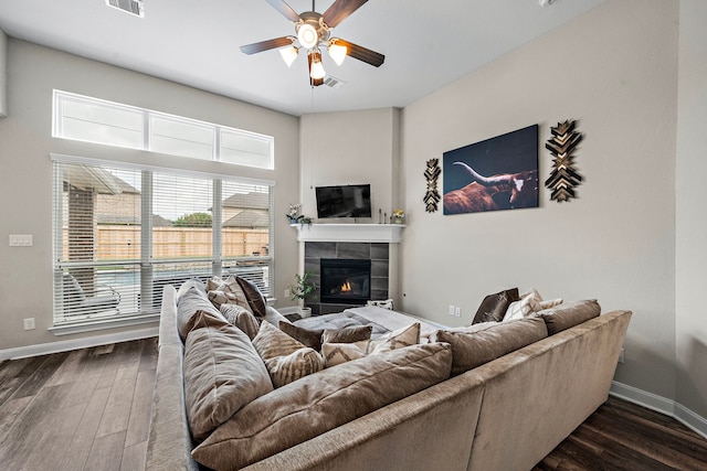 living area with dark wood-style flooring, a tiled fireplace, a ceiling fan, baseboards, and visible vents
