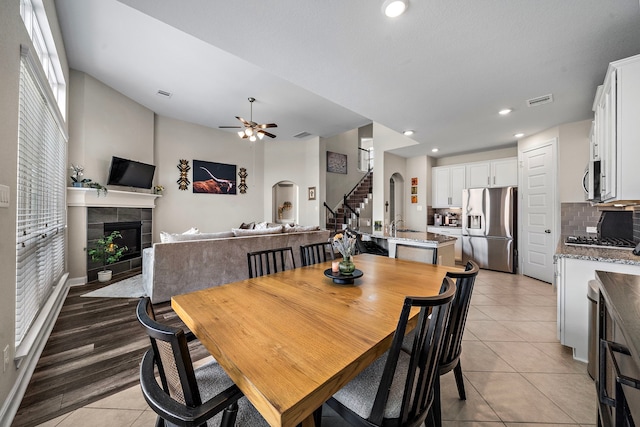 dining room featuring a ceiling fan, light tile patterned floors, a tile fireplace, visible vents, and stairway