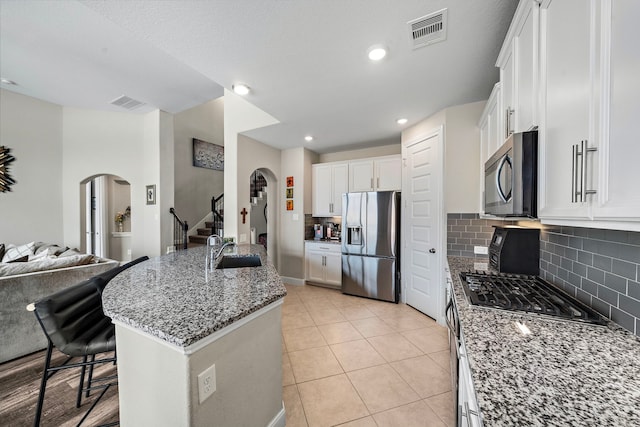 kitchen featuring white cabinets, appliances with stainless steel finishes, arched walkways, dark stone counters, and visible vents
