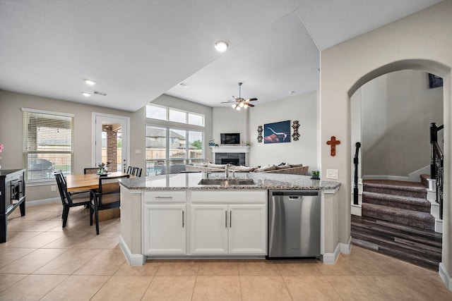 kitchen with a ceiling fan, stainless steel dishwasher, light stone countertops, a sink, and baseboards