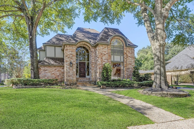 view of front facade featuring roof with shingles, a front yard, and brick siding