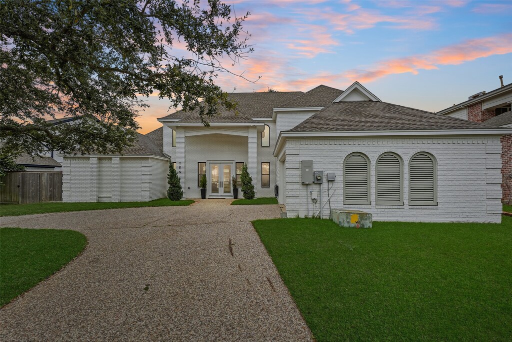 10 Quintana Pl, Galveston, TX 77554 - view of front of property with fence, roof with shingles, a front lawn, french doors, and driveway