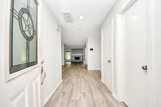 hallway with a textured ceiling, visible vents, baseboards, recessed lighting, and light wood-style flooring