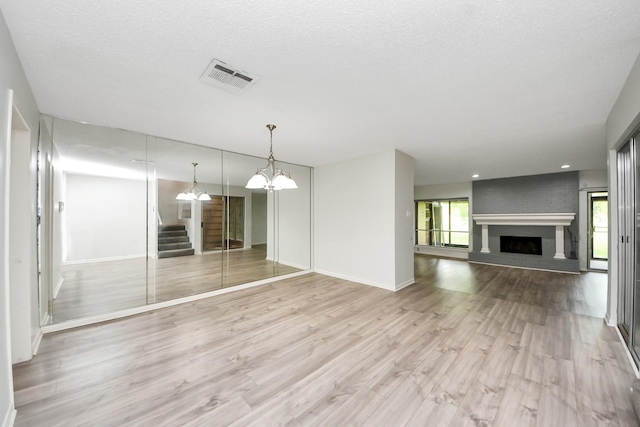 unfurnished living room featuring visible vents, a large fireplace, baseboards, a chandelier, and light wood-style flooring