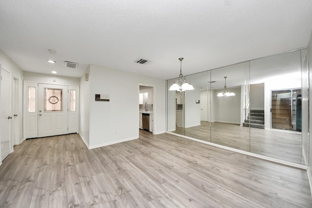 unfurnished living room featuring an inviting chandelier, stairway, light wood-style flooring, and visible vents