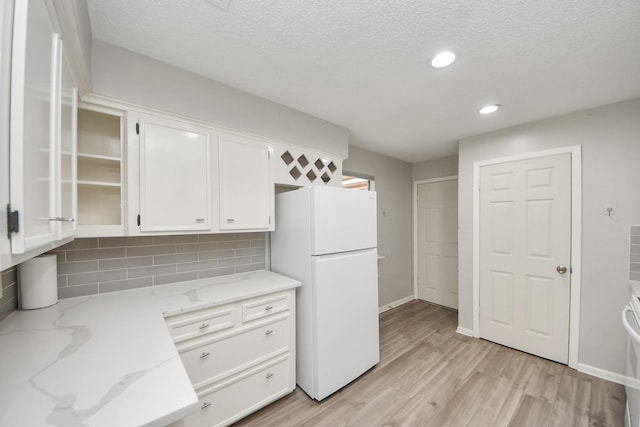 kitchen with decorative backsplash, white cabinets, freestanding refrigerator, and light wood finished floors