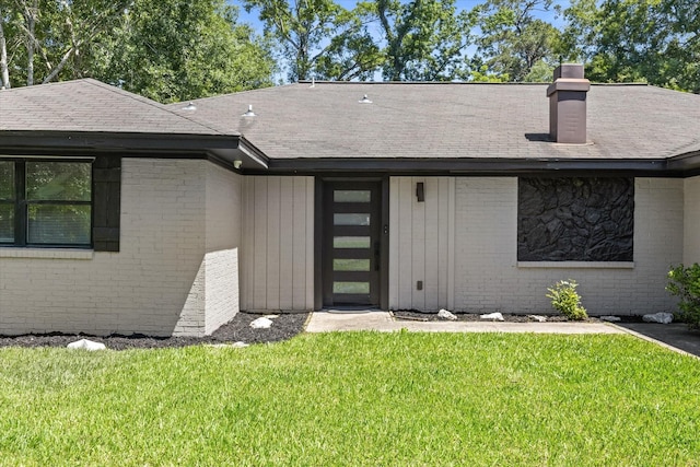 view of front of house with brick siding, a front yard, roof with shingles, and a chimney