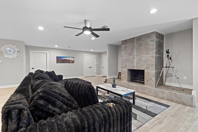living area featuring baseboards, light wood-type flooring, recessed lighting, ceiling fan, and a fireplace
