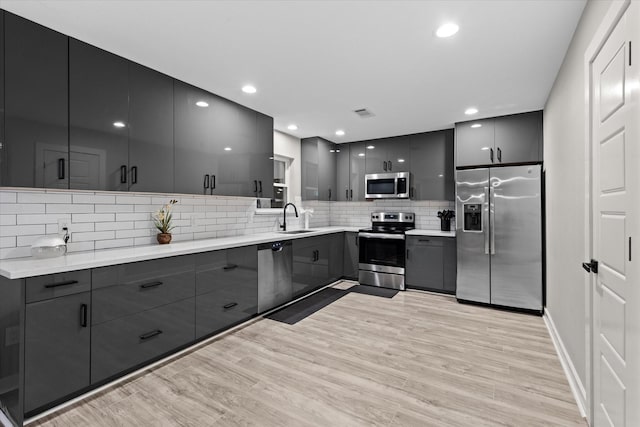 kitchen featuring stainless steel appliances, a sink, modern cabinets, light wood-type flooring, and gray cabinetry