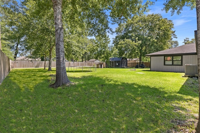 view of yard featuring a trampoline, an outbuilding, a storage unit, and central AC