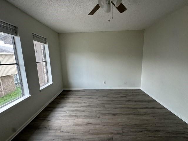 empty room featuring baseboards, a ceiling fan, dark wood finished floors, and a textured ceiling