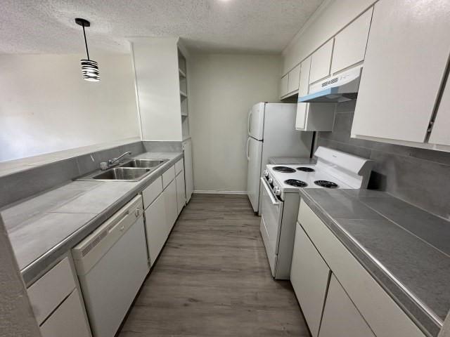 kitchen with white appliances, a textured ceiling, under cabinet range hood, and a sink