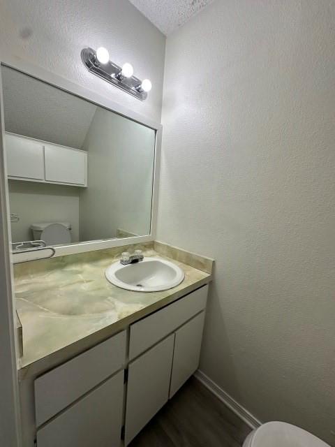 bathroom featuring a textured ceiling, wood finished floors, vanity, baseboards, and toilet