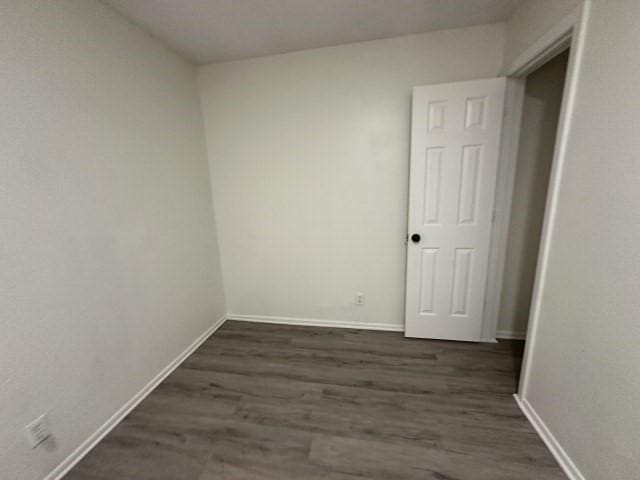 unfurnished room with baseboards and dark wood-type flooring