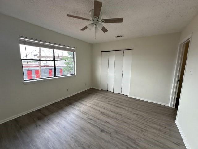 unfurnished bedroom with a textured ceiling, visible vents, wood finished floors, baseboards, and a closet
