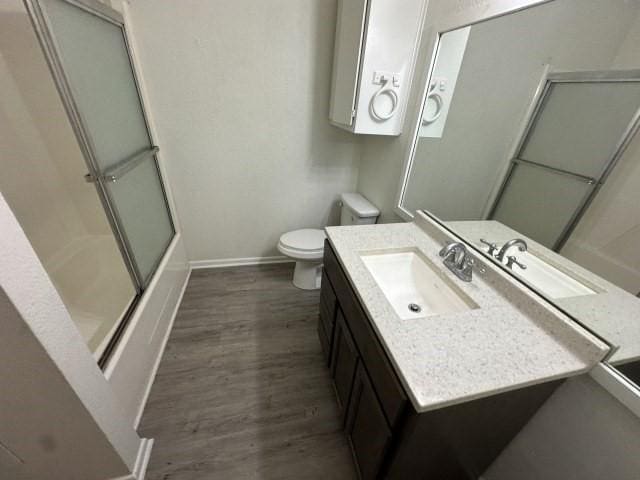 full bathroom with shower / bath combination with glass door, vanity, toilet, baseboards, and wood finished floors