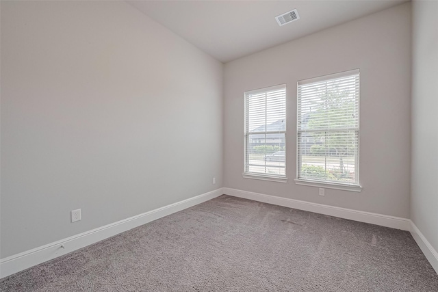 spare room featuring baseboards, visible vents, vaulted ceiling, and dark colored carpet