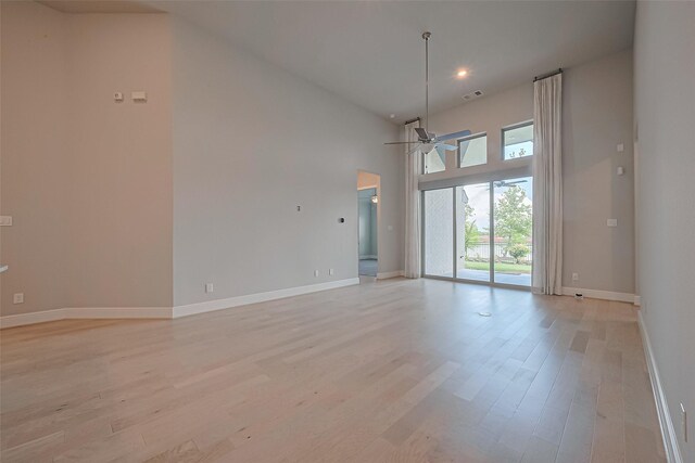 unfurnished room with ceiling fan, visible vents, a towering ceiling, light wood-type flooring, and baseboards
