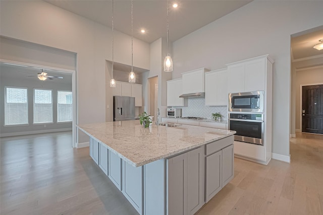kitchen with appliances with stainless steel finishes, light wood-style floors, a towering ceiling, backsplash, and a spacious island