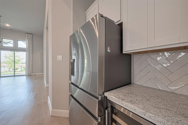 kitchen with stainless steel refrigerator with ice dispenser, baseboards, white cabinetry, and tasteful backsplash