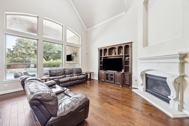 living room with crown molding, a fireplace, dark wood finished floors, high vaulted ceiling, and baseboards
