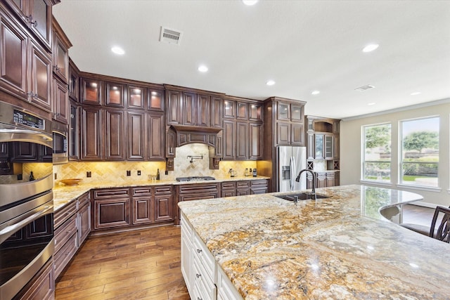 kitchen with visible vents, appliances with stainless steel finishes, a sink, glass insert cabinets, and dark wood-type flooring