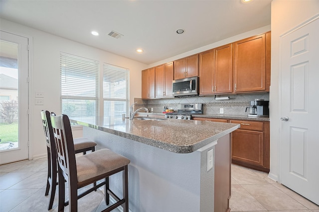 kitchen featuring visible vents, decorative backsplash, a kitchen bar, appliances with stainless steel finishes, and light tile patterned floors