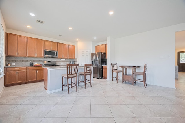 kitchen with a breakfast bar area, a kitchen island, backsplash, visible vents, and appliances with stainless steel finishes