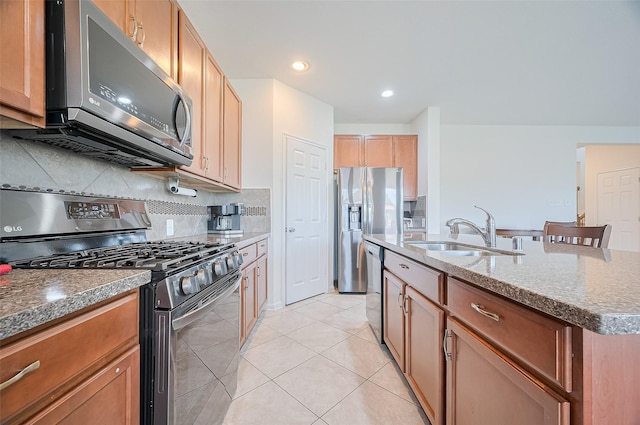 kitchen featuring a sink, dark stone countertops, stainless steel appliances, tasteful backsplash, and a center island with sink