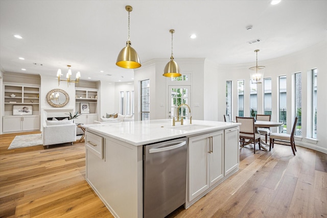 kitchen with stainless steel dishwasher, light wood-type flooring, visible vents, a sink, and an island with sink
