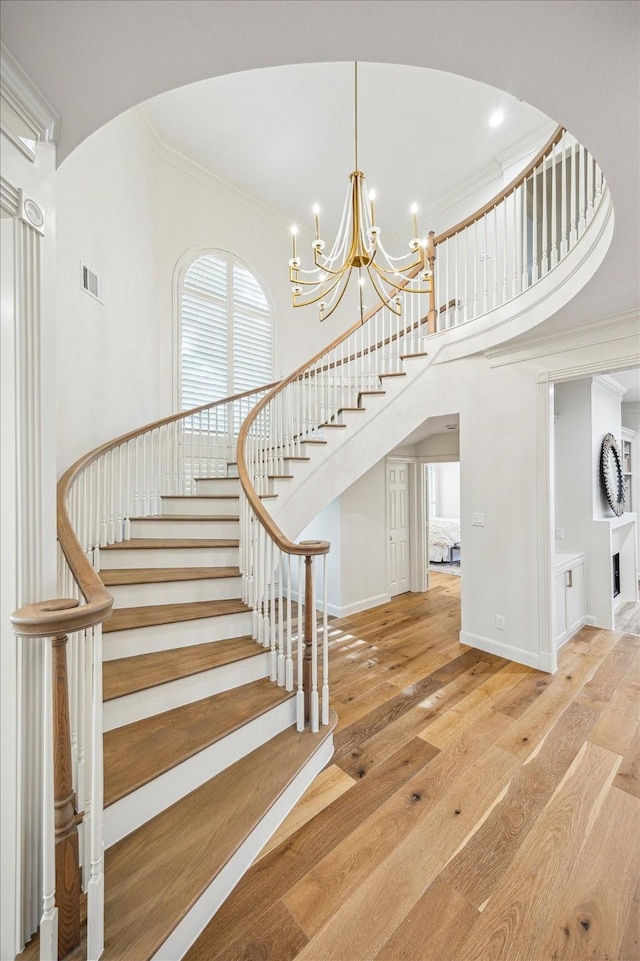 staircase with a notable chandelier, baseboards, crown molding, wood finished floors, and a high ceiling