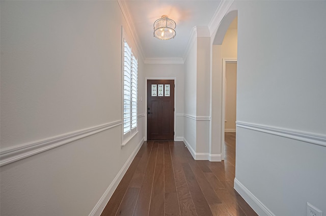 doorway with an inviting chandelier, ornamental molding, baseboards, arched walkways, and dark wood finished floors