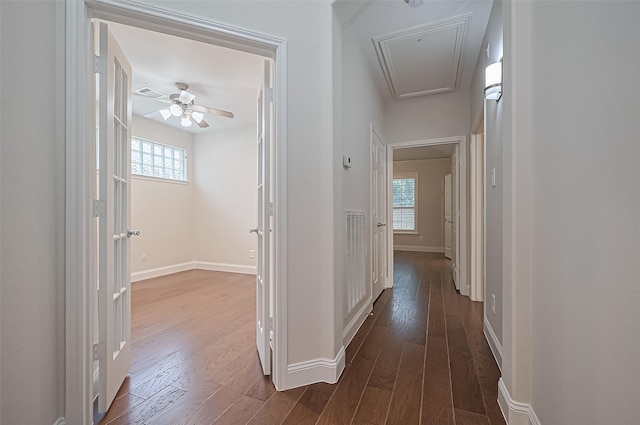 hallway featuring baseboards, attic access, dark wood finished floors, and a healthy amount of sunlight
