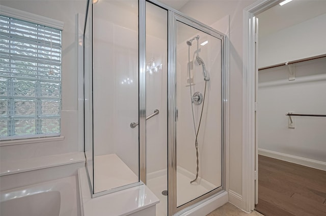 bathroom with baseboards, a wealth of natural light, wood finished floors, a spacious closet, and a stall shower