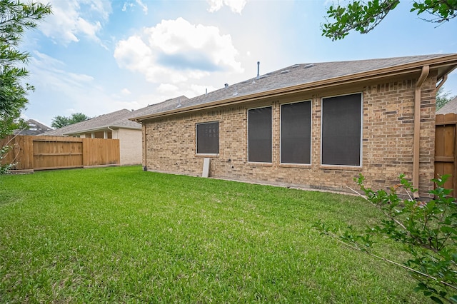 back of property featuring brick siding, roof with shingles, fence, and a yard
