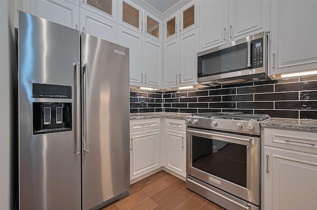 kitchen featuring white cabinetry, premium appliances, light stone countertops, and tasteful backsplash