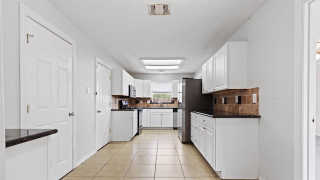 kitchen featuring stainless steel appliances, white cabinetry, light tile patterned floors, and tasteful backsplash