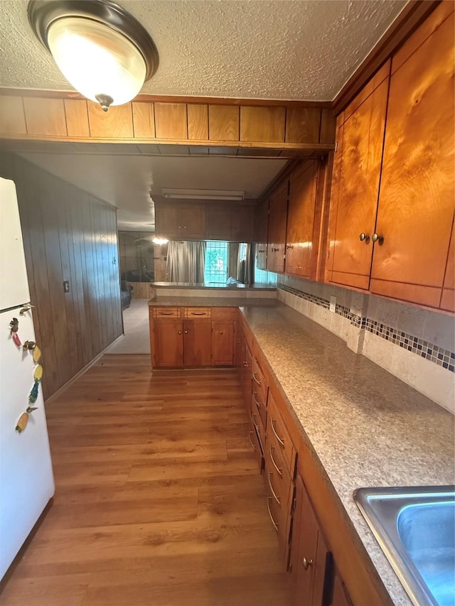 4300 Weaver Rd, Houston, TX 77016 - kitchen with brown cabinetry, a textured ceiling, wood walls, freestanding refrigerator, and light wood finished floors