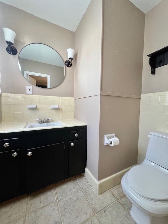 half bathroom featuring tile patterned floors, vanity, toilet, and tile walls