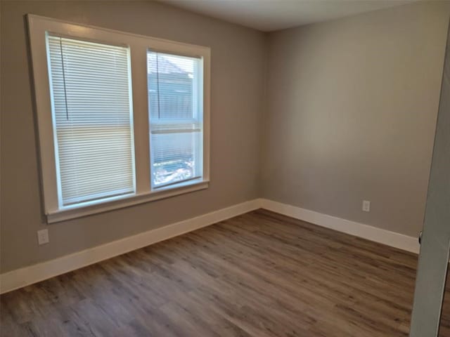 spare room with baseboards and dark wood-type flooring