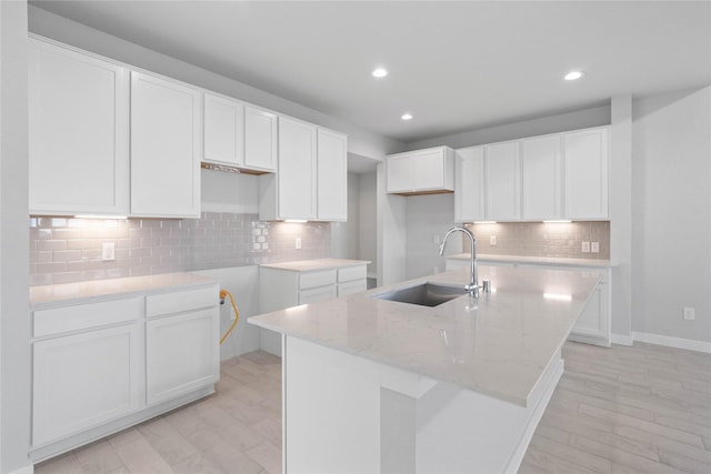 kitchen featuring recessed lighting, a sink, a kitchen island with sink, and light stone counters